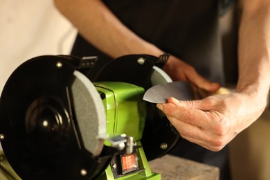 Photo of Man sharpening knife with bench grinder indoors, closeup