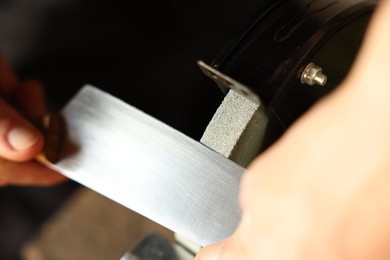 Photo of Man sharpening knife with bench grinder indoors, closeup
