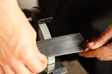 Photo of Man sharpening knife with bench grinder indoors, closeup