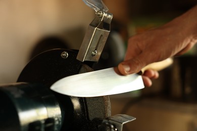 Photo of Man sharpening knife with bench grinder indoors, closeup