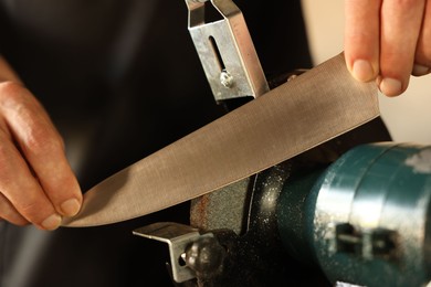 Photo of Man sharpening knife with bench grinder indoors, closeup