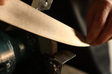 Photo of Man sharpening knife with bench grinder indoors, closeup