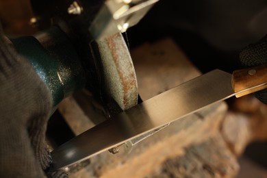 Photo of Man sharpening knife with bench grinder indoors, above view