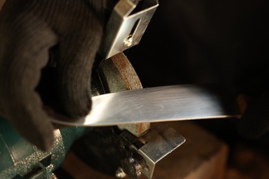 Photo of Man sharpening knife with bench grinder indoors, closeup