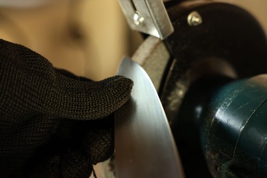 Photo of Man sharpening knife with bench grinder indoors, closeup