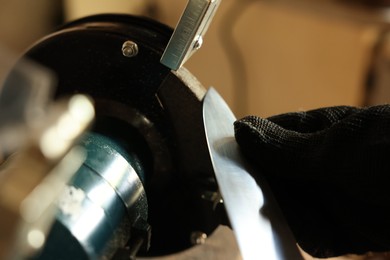 Photo of Man sharpening knife with bench grinder indoors, closeup
