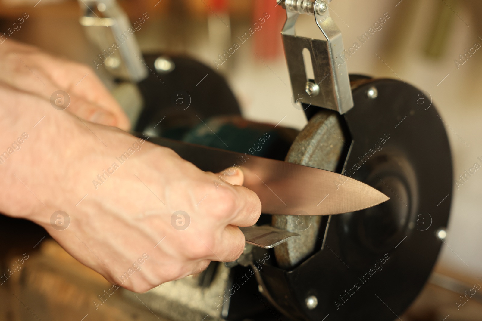 Man sharpening knife with bench grinder indoors, closeup Photo of Man sharpening knife with bench grinder indoors, closeup