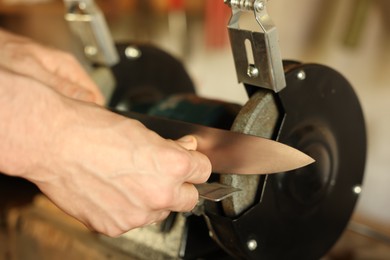 Photo of Man sharpening knife with bench grinder indoors, closeup