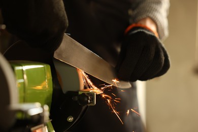 Photo of Man sharpening knife with bench grinder indoors, closeup