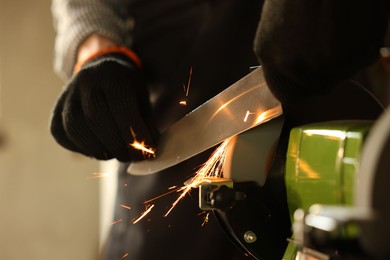 Photo of Man sharpening knife with bench grinder indoors, closeup
