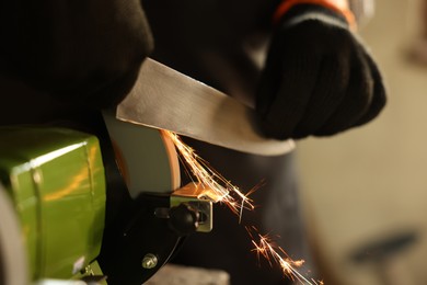 Photo of Man sharpening knife with bench grinder indoors, closeup