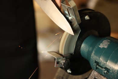 Photo of Man sharpening knife with bench grinder indoors, closeup. Space for text