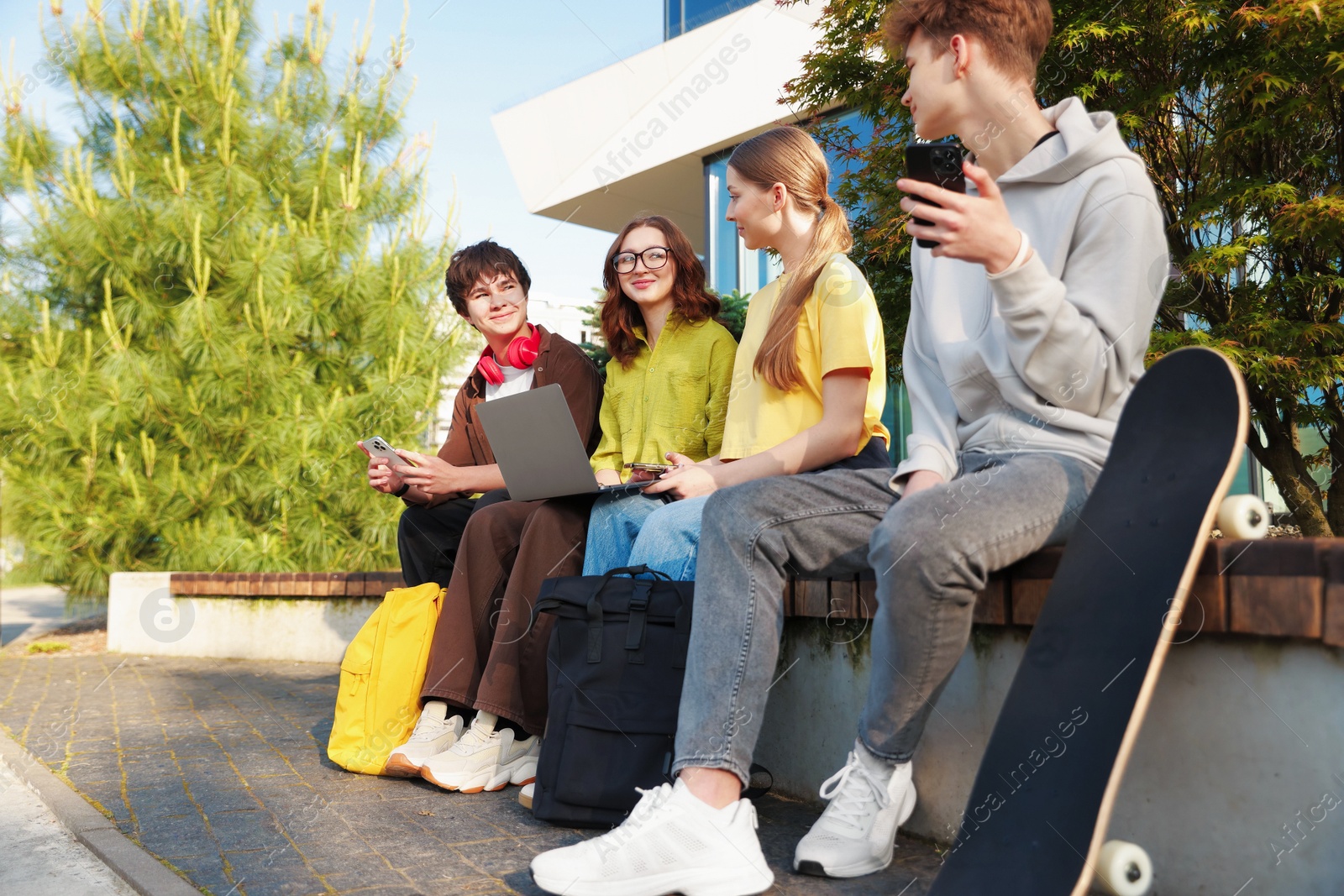 Teenagers with different devices on bench in park Photo of Teenagers with different devices on bench in park