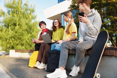 Photo of Teenagers with different devices on bench in park