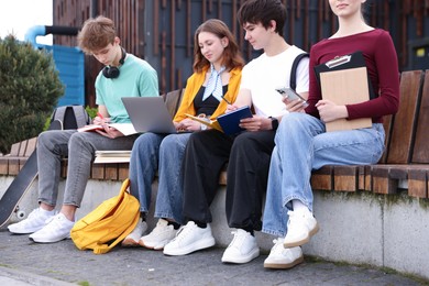 Photo of Group of teenagers studying together on bench outdoors