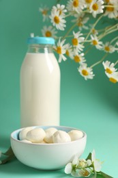 Photo of Fresh milk in glass bottle, mozzarella balls and flowers on turquoise background, closeup. Dairy products
