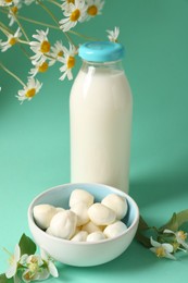 Photo of Fresh milk in glass bottle, mozzarella balls and flowers on turquoise background, closeup. Dairy products