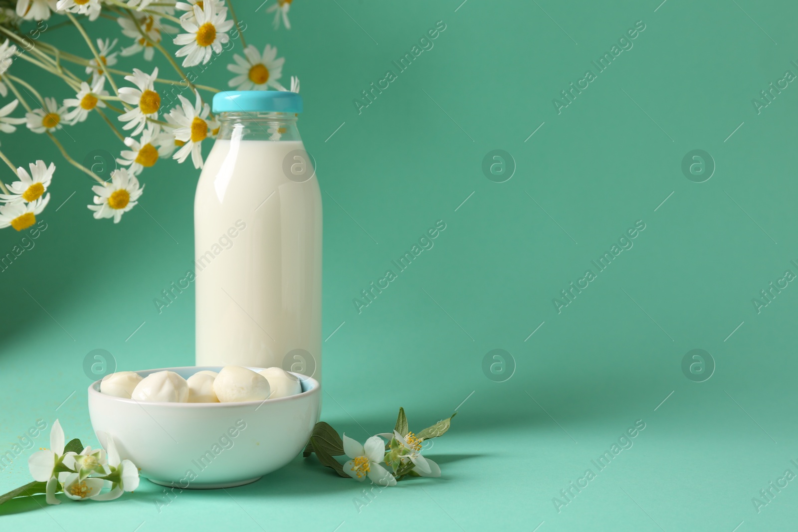 Photo of Fresh milk in glass bottle, mozzarella balls and flowers on turquoise background, space for text. Dairy products