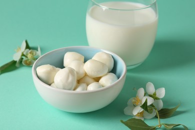 Photo of Fresh milk in glass, mozzarella balls and flowers on turquoise background, closeup. Dairy products