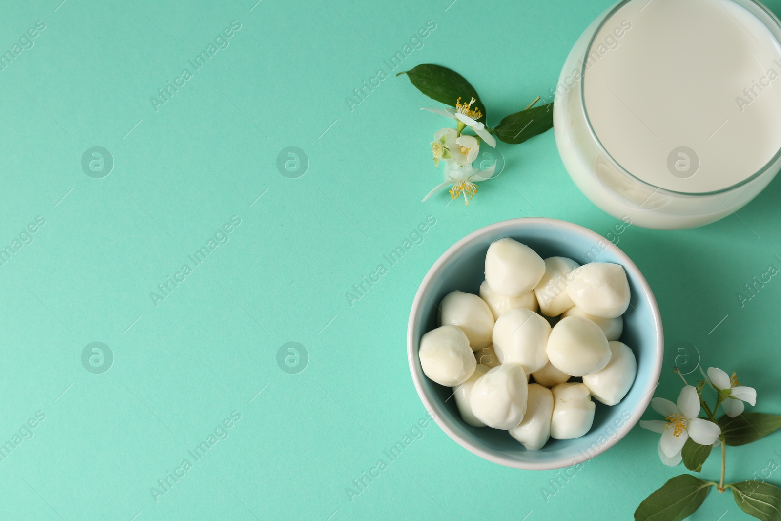 Photo of Dairy products. Fresh milk in glass, mozzarella balls and flowers on turquoise background, flat lay. Space for text