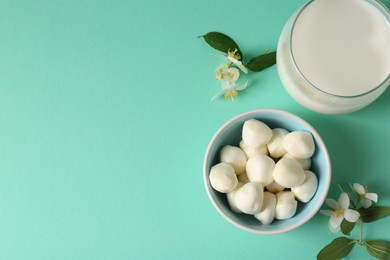 Photo of Dairy products. Fresh milk in glass, mozzarella balls and flowers on turquoise background, flat lay. Space for text