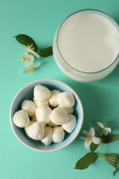 Photo of Fresh milk in glass, mozzarella balls and flowers on turquoise background, flat lay. Dairy products