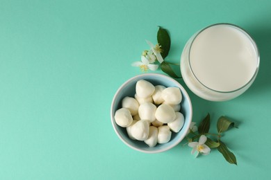 Photo of Dairy products. Fresh milk in glass, mozzarella balls and flowers on turquoise background, flat lay. Space for text