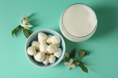 Photo of Fresh milk in glass, mozzarella balls and flowers on turquoise background, flat lay. Dairy products