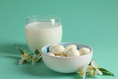 Photo of Fresh milk in glass, mozzarella balls and flowers on turquoise background, closeup. Dairy products