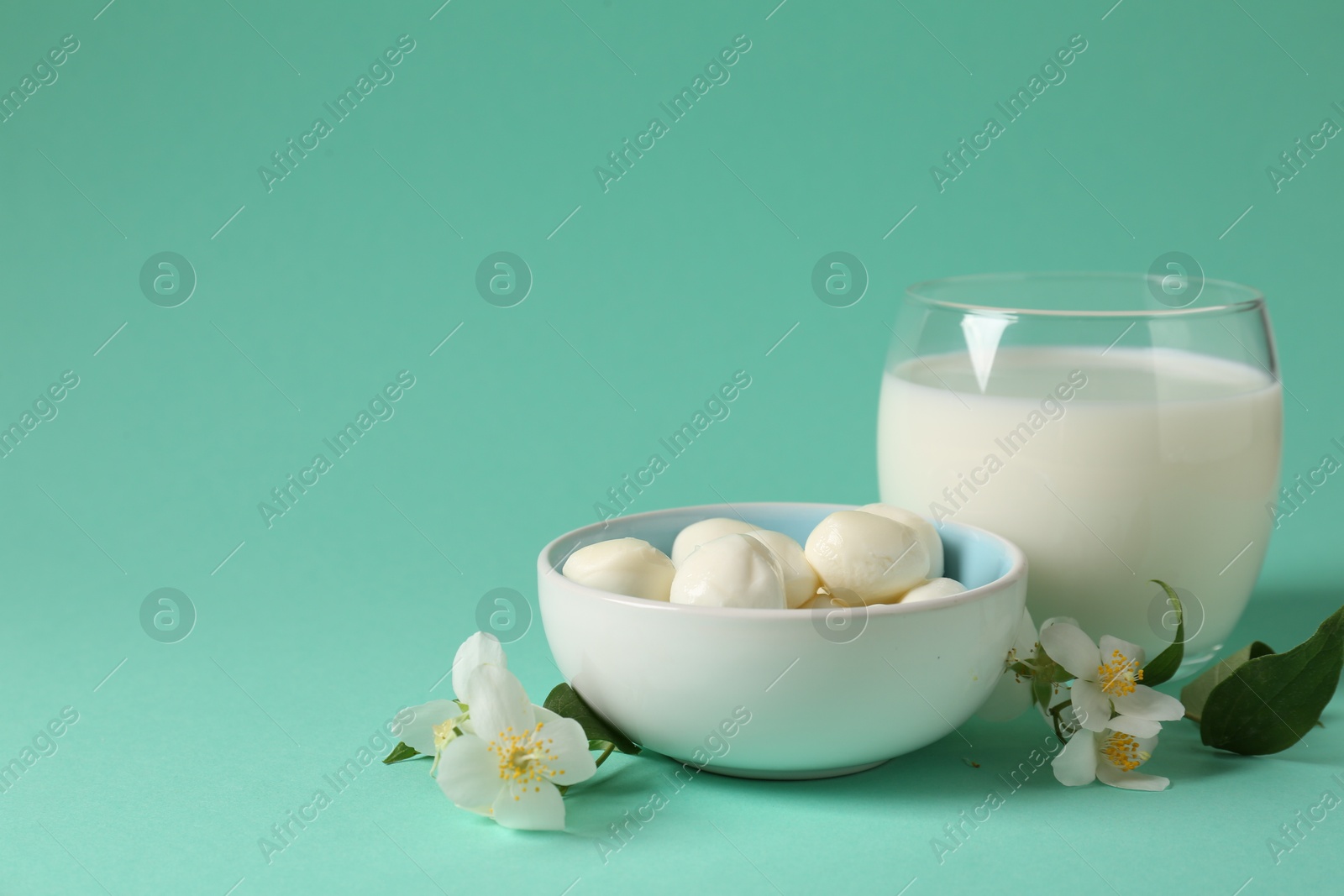 Photo of Fresh milk in glass, mozzarella balls and flowers on turquoise background, space for text. Dairy products