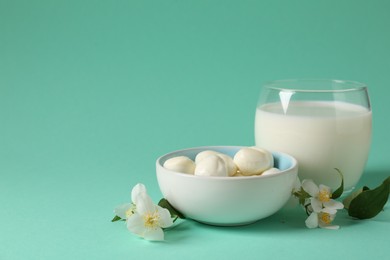 Photo of Fresh milk in glass, mozzarella balls and flowers on turquoise background, space for text. Dairy products