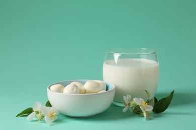 Photo of Fresh milk in glass, mozzarella balls and flowers on turquoise background. Dairy products