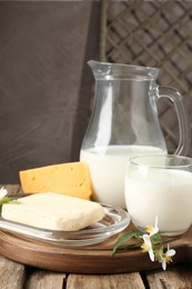 Photo of Different fresh dairy products and flowers on wooden table, closeup