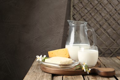 Photo of Different fresh dairy products and flowers on wooden table, space for text