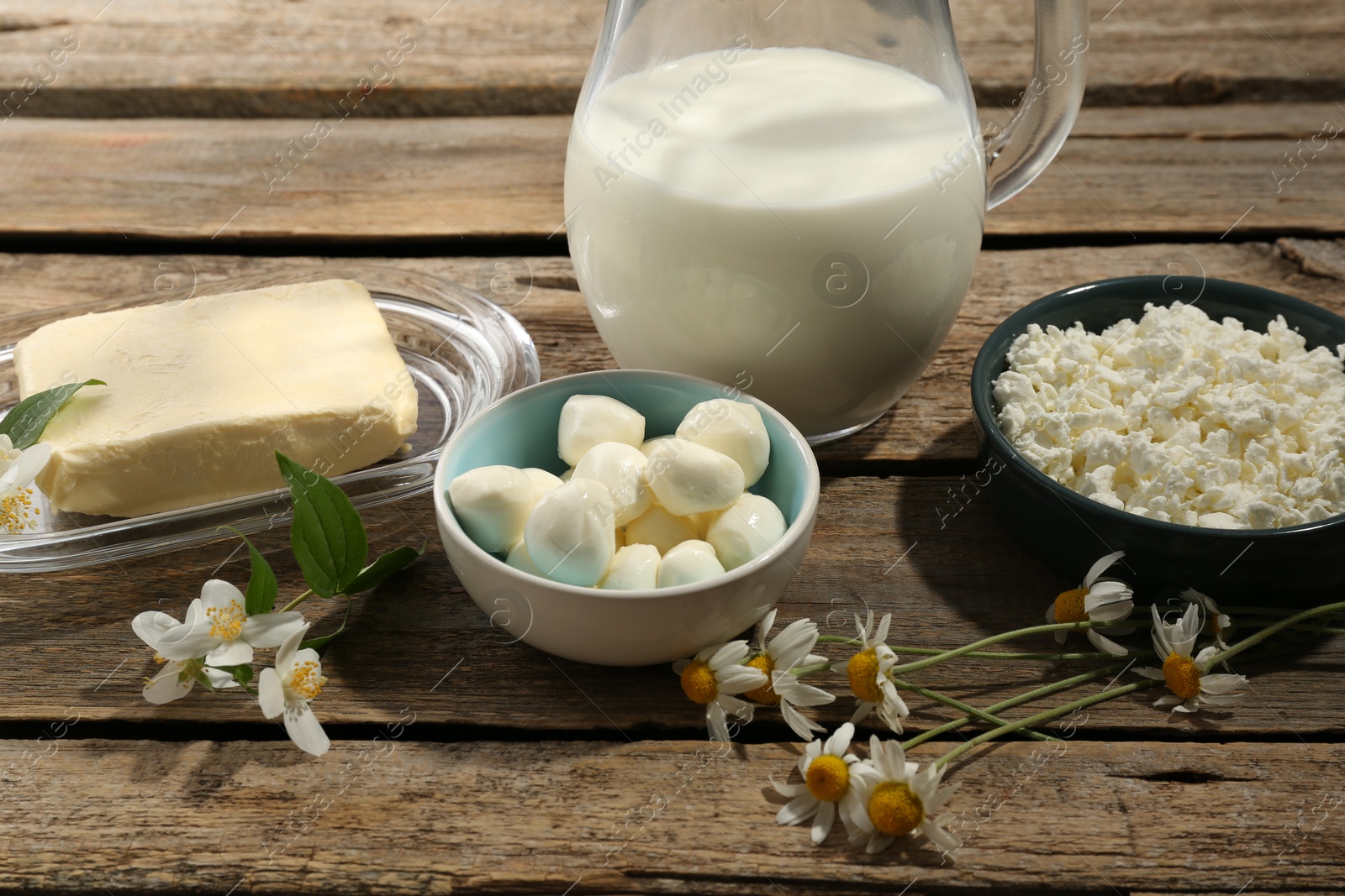 Photo of Different fresh dairy products and flowers on wooden table