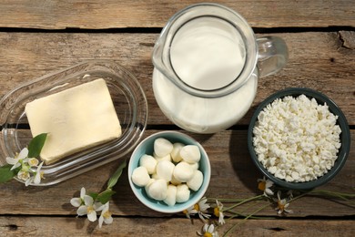 Photo of Different fresh dairy products and flowers on wooden table, flat lay