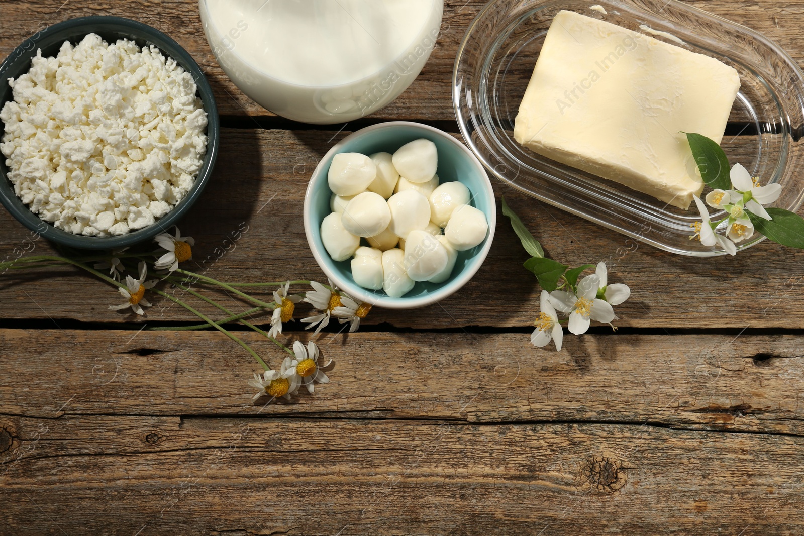 Photo of Different fresh dairy products and flowers on wooden table, flat lay. Space for text