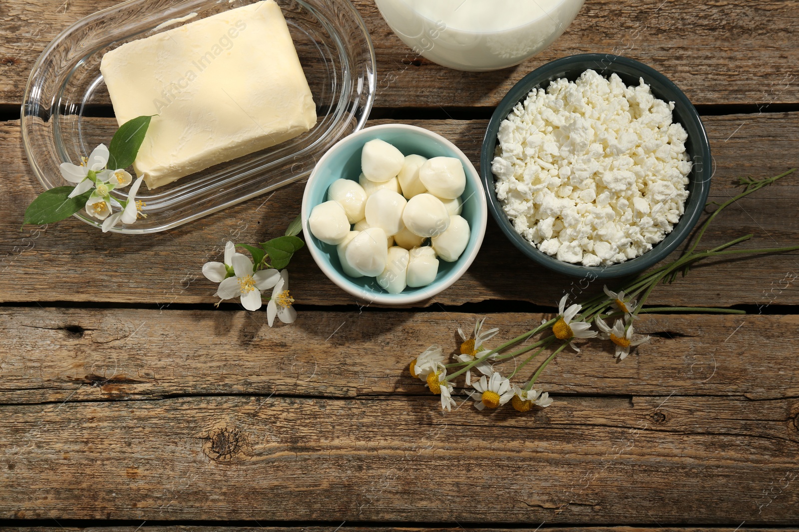 Photo of Different fresh dairy products and flowers on wooden table, flat lay. Space for text