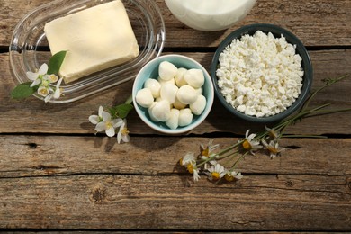 Photo of Different fresh dairy products and flowers on wooden table, flat lay. Space for text