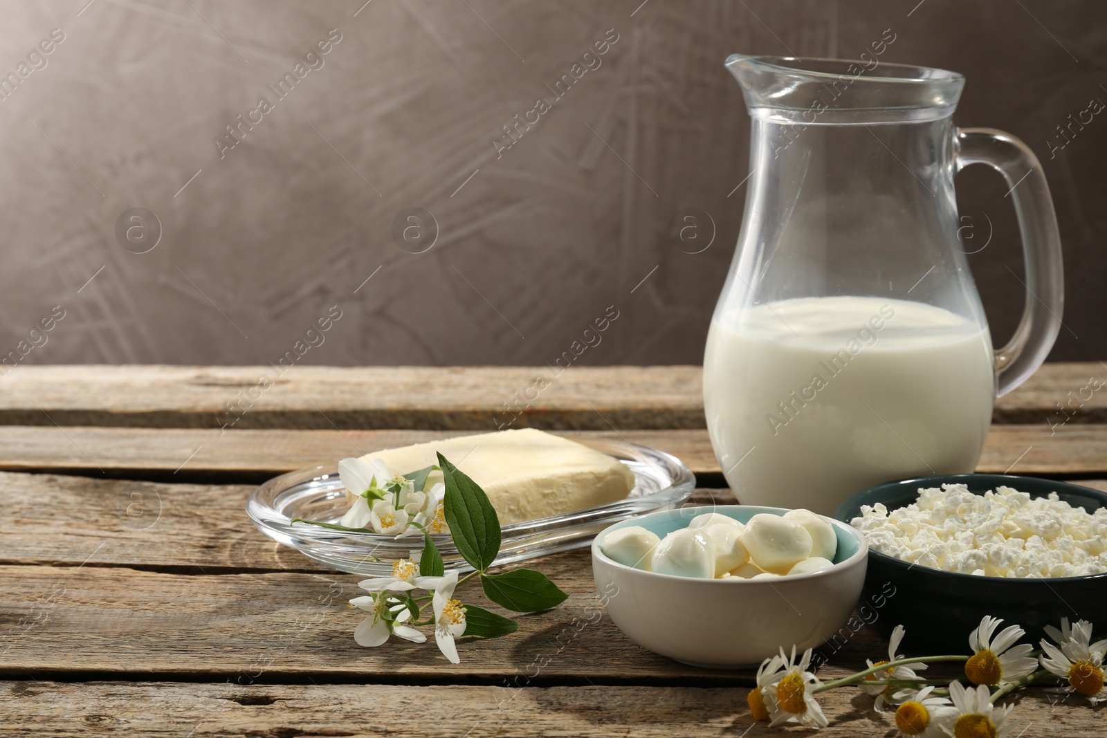 Photo of Different fresh dairy products and flowers on wooden table, space for text
