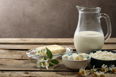 Photo of Different fresh dairy products and flowers on wooden table, space for text