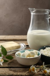 Photo of Different fresh dairy products and flowers on wooden table, closeup