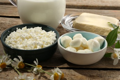 Photo of Different fresh dairy products and flowers on wooden table, closeup