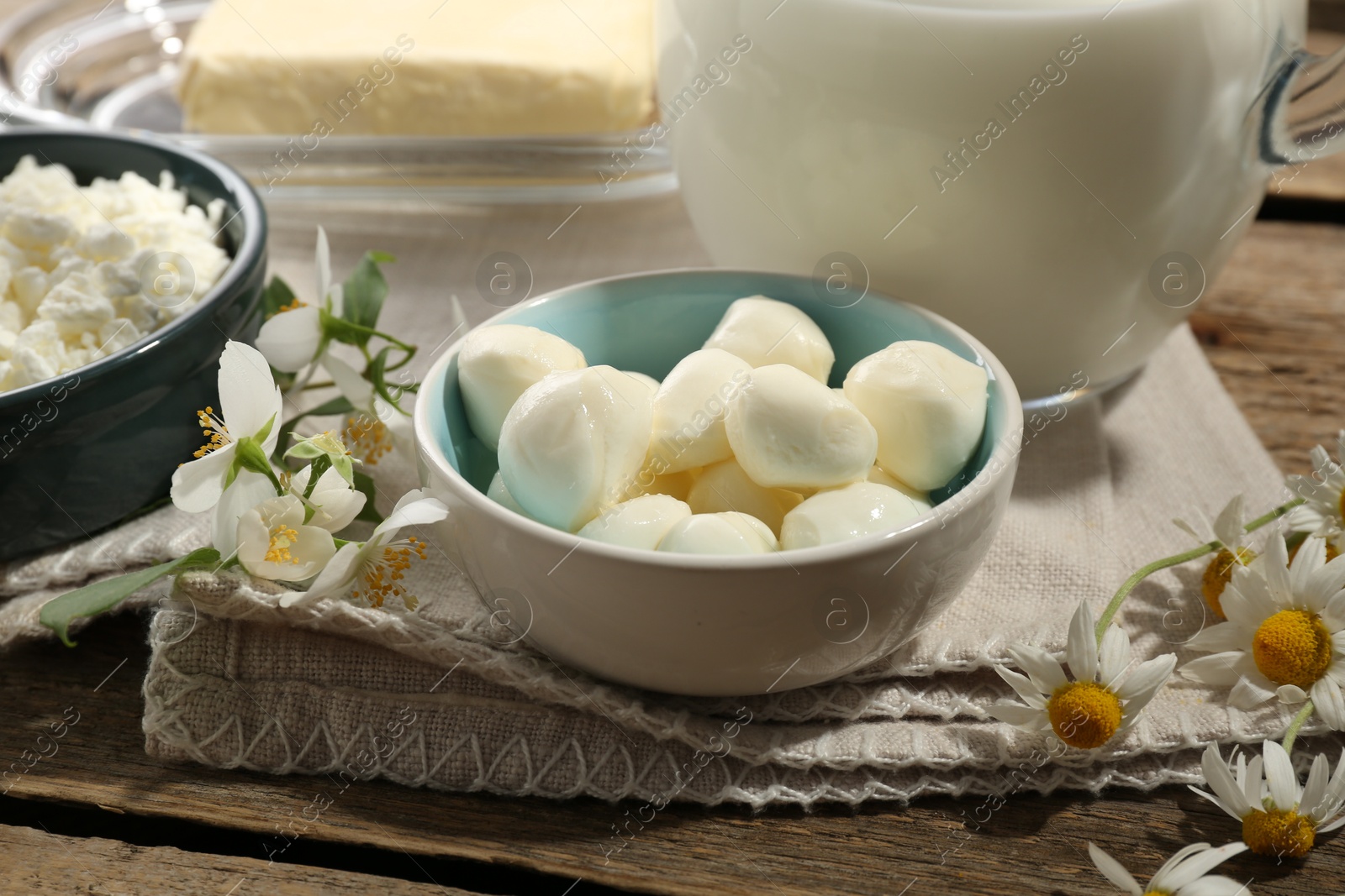 Photo of Different fresh dairy products and flowers on wooden table, closeup