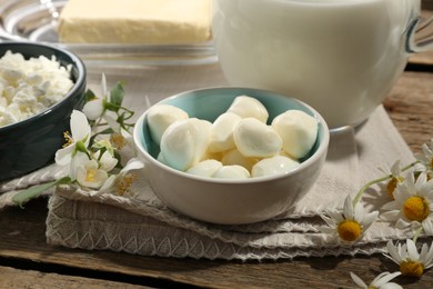 Photo of Different fresh dairy products and flowers on wooden table, closeup