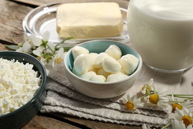 Photo of Different fresh dairy products and flowers on wooden table, closeup