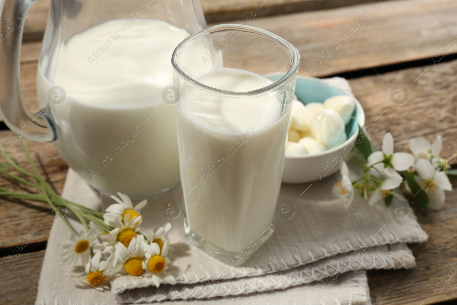Photo of Fresh milk, mozzarella balls and flowers on wooden table, closeup. Dairy products