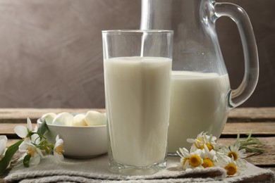 Photo of Fresh milk, mozzarella balls and flowers on wooden table, closeup. Dairy products
