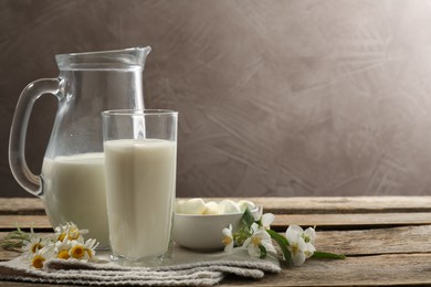 Photo of Fresh milk, mozzarella balls and flowers on wooden table, space for text. Dairy products