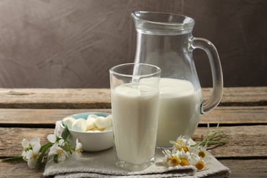 Photo of Fresh milk, mozzarella balls and flowers on wooden table, closeup. Dairy products